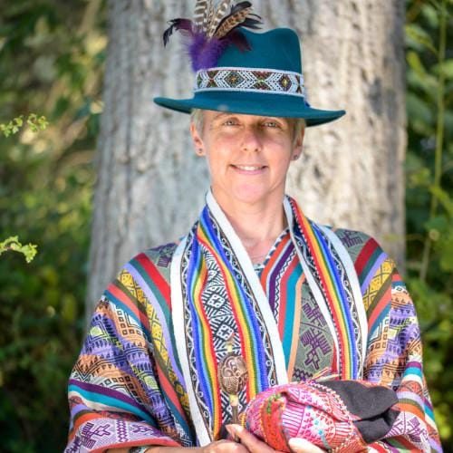 Ali shamanic services homepage pic 500px Ali Rabjohns wearing brightly coloured ceremonial robes from the Peruvian tradition while holding a mesa, in sunlight